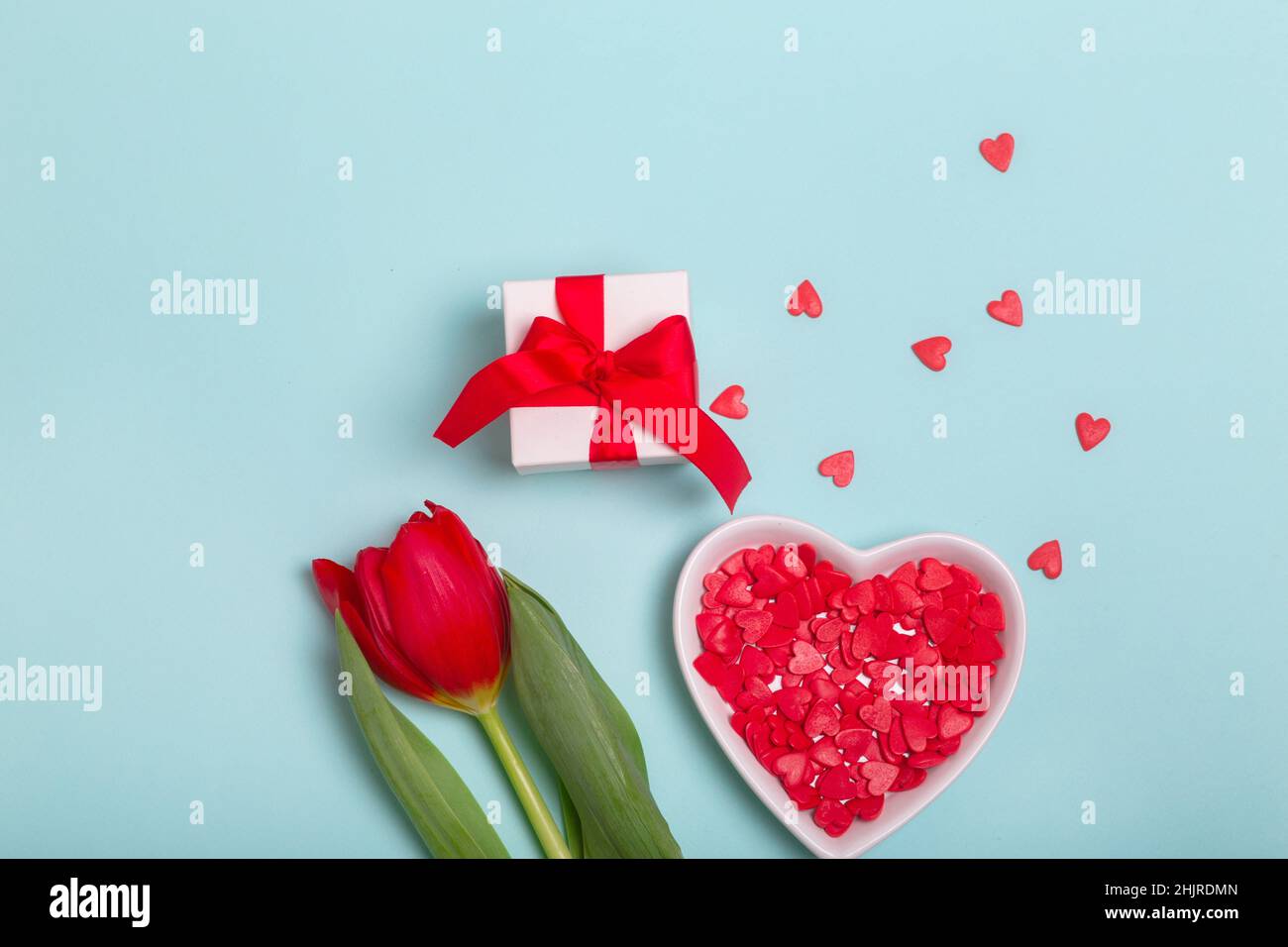 Boîte cadeau artisanale avec ruban rouge, fleurs et coeurs en papier sur fond bleu pour la Saint-Valentin. Fête des mères. Banque D'Images