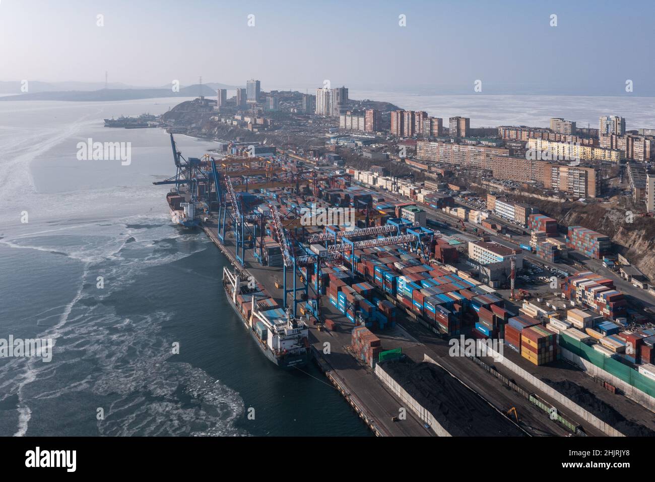 Vladivostok, Russie - 27 janvier 2022 : Vue de dessus du terminal des conteneurs du port maritime et de la ville.En hiver, un bateau à conteneurs est en train de charger au quai. Banque D'Images