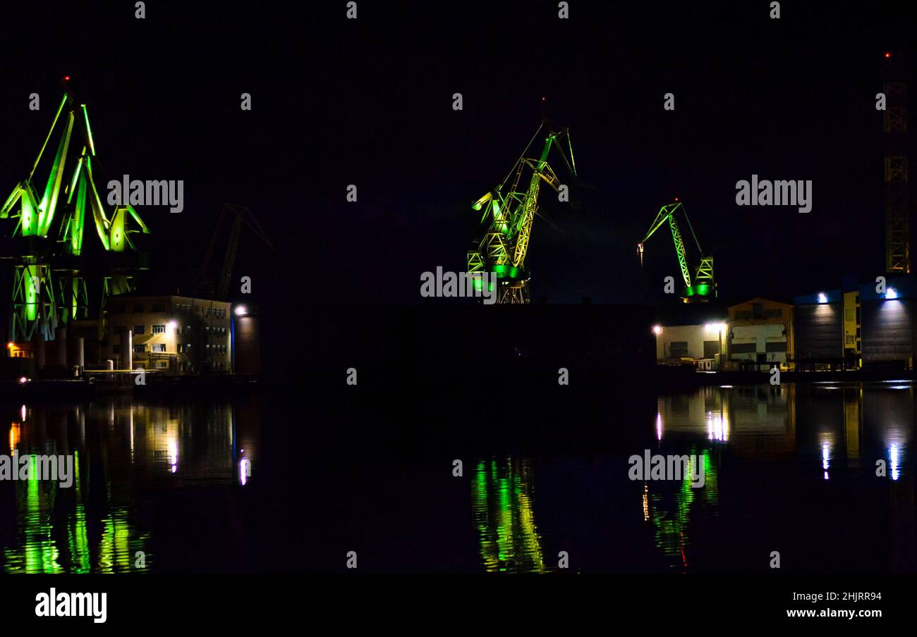 Grands grues illuminées au chantier naval Pula en Croatie la nuit.Les couleurs vertes reflètent les eaux sombres du port.LA chorégraphie DE la LUMIÈRE LED. Banque D'Images