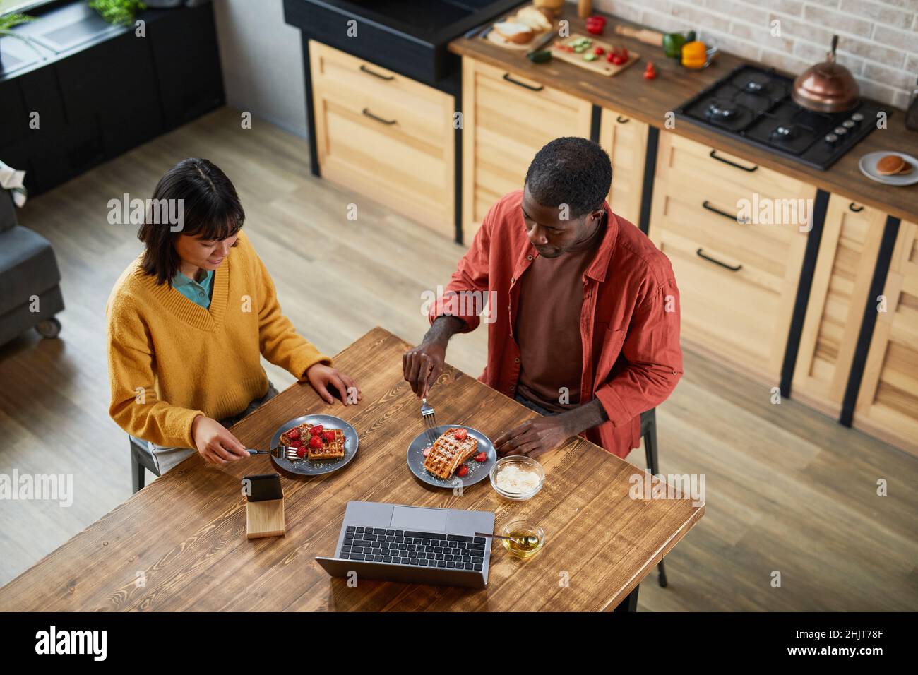 Vue de dessus portrait de jeune couple mixte de course appréciant le petit déjeuner dans la cuisine maison confortable, espace de copie Banque D'Images