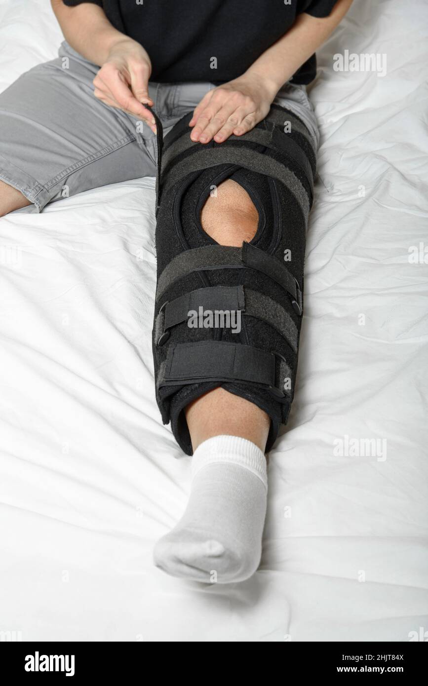 Femme fixant l'orthèse de Velcro réglable sur une jambe cassée assise dans le lit.Port d'une jambe de force après une blessure.Gros plan.Orientation verticale Banque D'Images