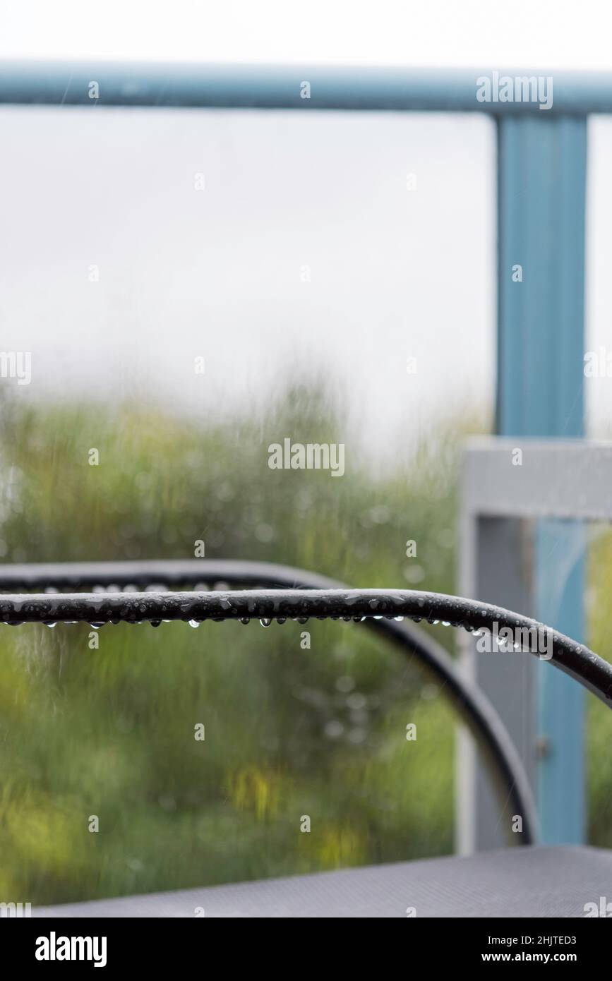 Une image concept d'un les bras d'une chaise extérieure et d'une table, s'égoutter humide sous la pluie avec un fond en verre flou Banque D'Images