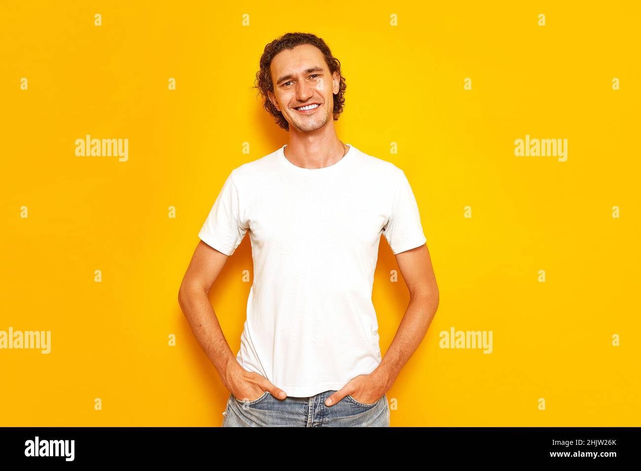 Homme en T-shirt blanc décontracté debout sur un fond jaune isolé garde ses mains dans ses poches Banque D'Images