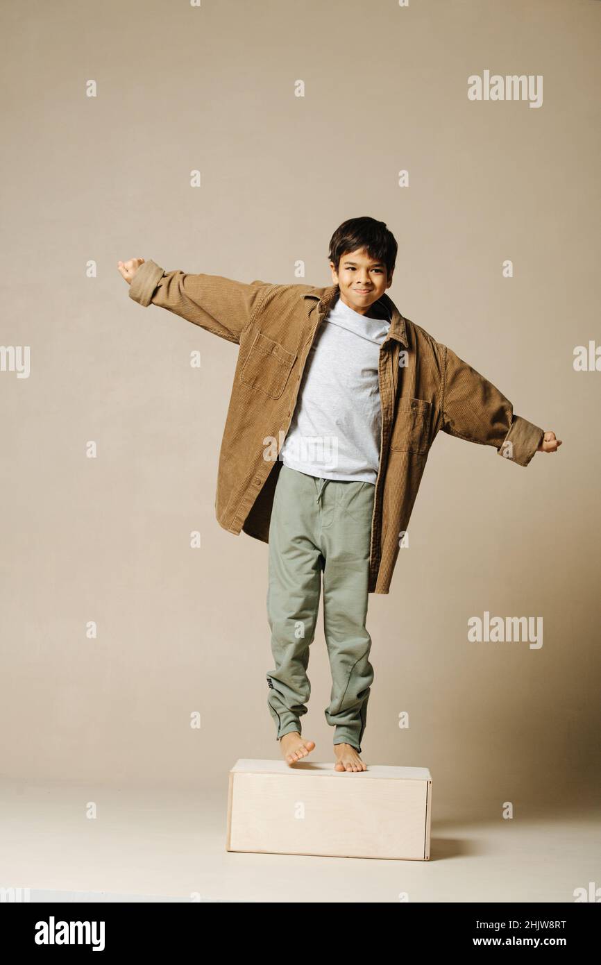 Etendre les mains de l'Indien garçon dans la chemise beige à manches  longues surdimensionnées debout sur un pied de boîte.Sur fond beige Photo  Stock - Alamy