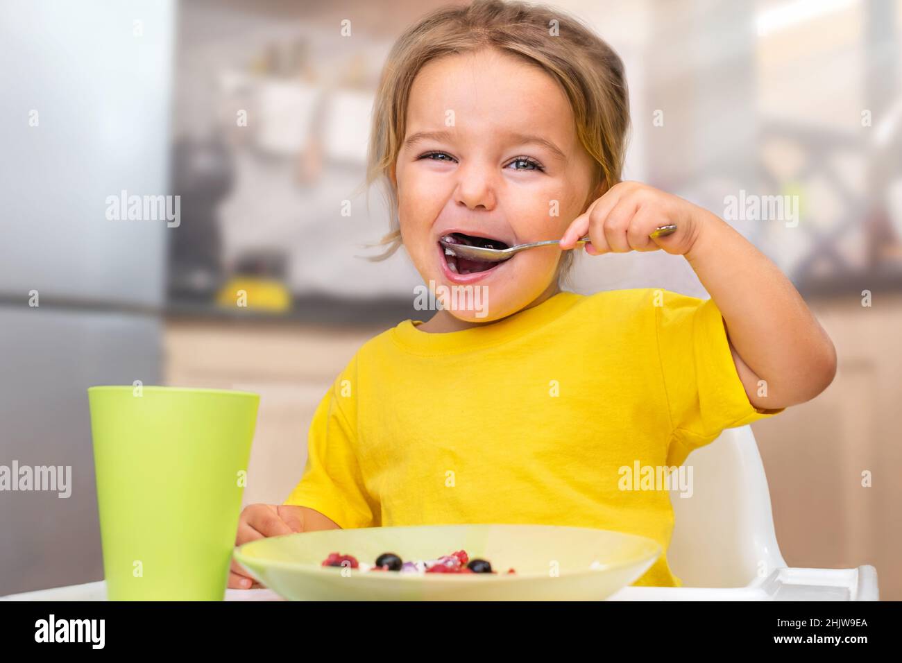 Enfant mangeant du porridge avec des baies dans une chaise haute dans la cuisine Banque D'Images