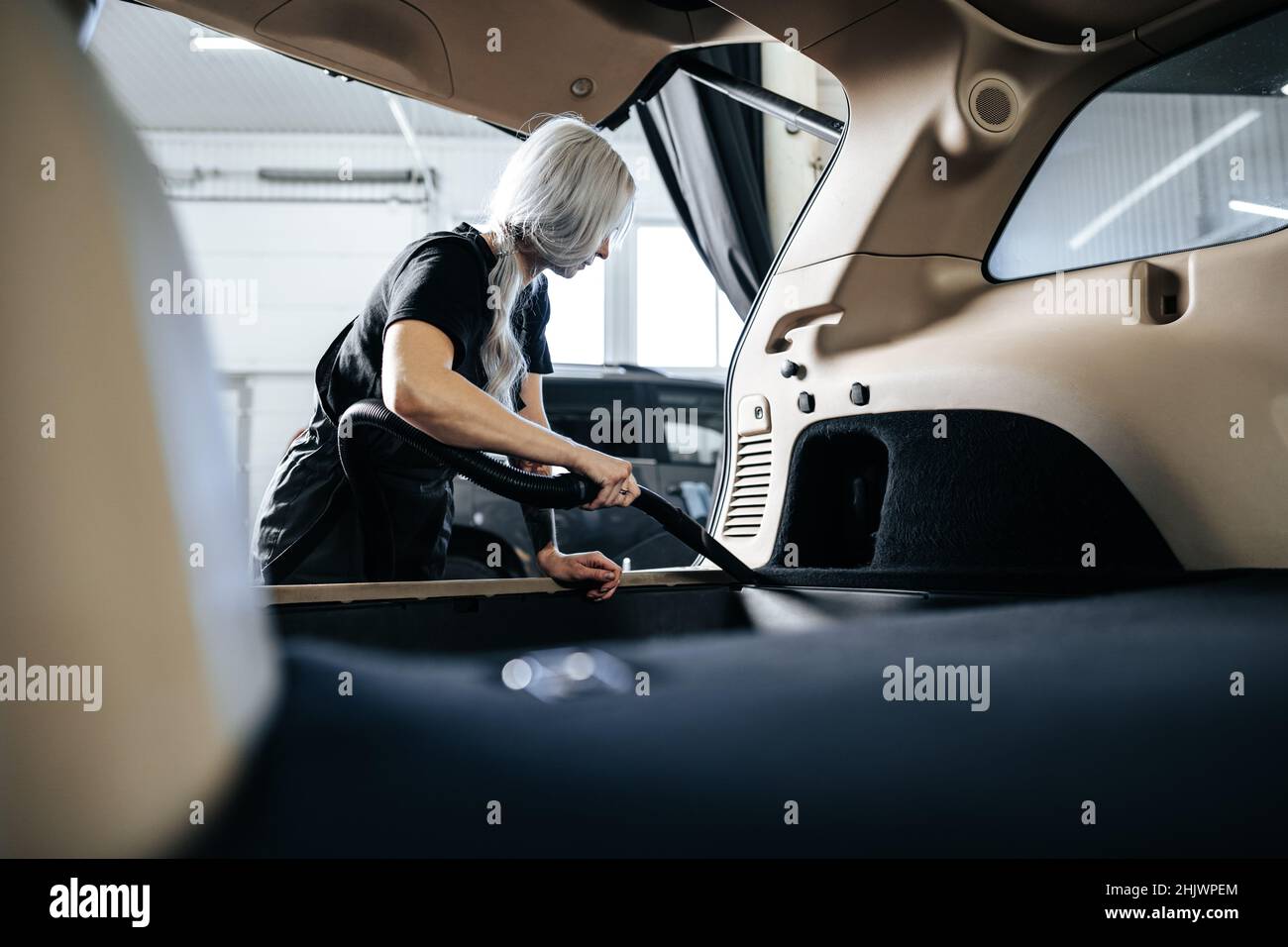 Femme travailleuse aspirant poussière intérieur de la voiture dans le lave-auto. Banque D'Images