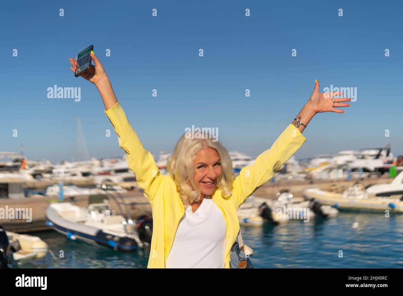 Voyageur femme levant les bras tenant un smartphone avec un passeport numérique de santé Banque D'Images