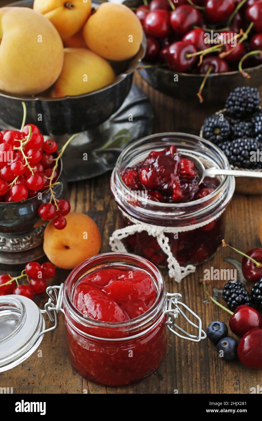 Pots de confiture de fraises de cerise parmi les fruits d'été et d'automne sur une table en bois. Banque D'Images