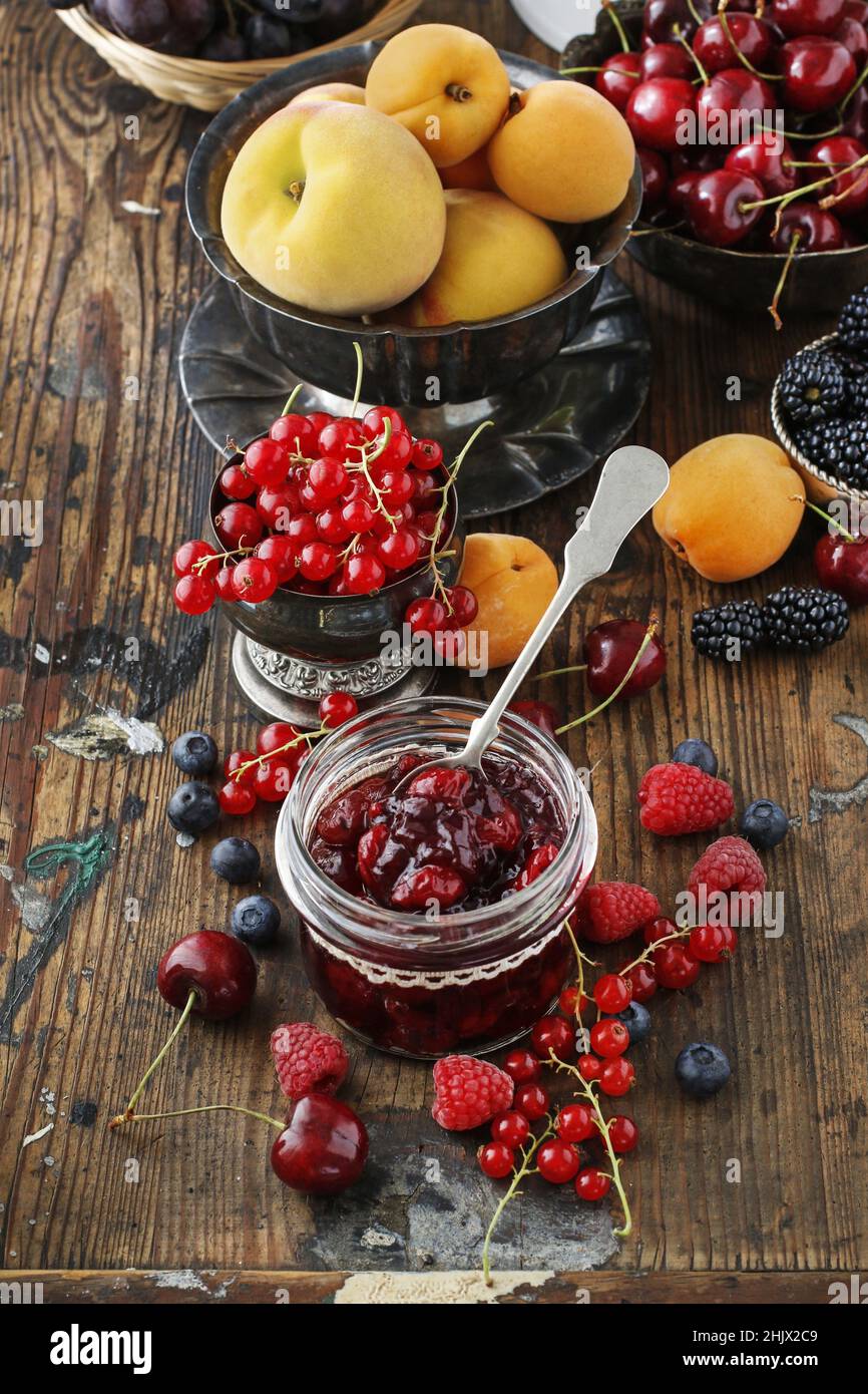 Pots de confiture de fraises de cerise parmi les fruits d'été et d'automne sur une table en bois. Banque D'Images