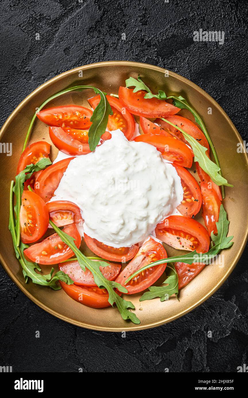 Salade italienne caprese avec fromage stracciatella, tomates et arugula.Arrière-plan noir.Vue de dessus Banque D'Images