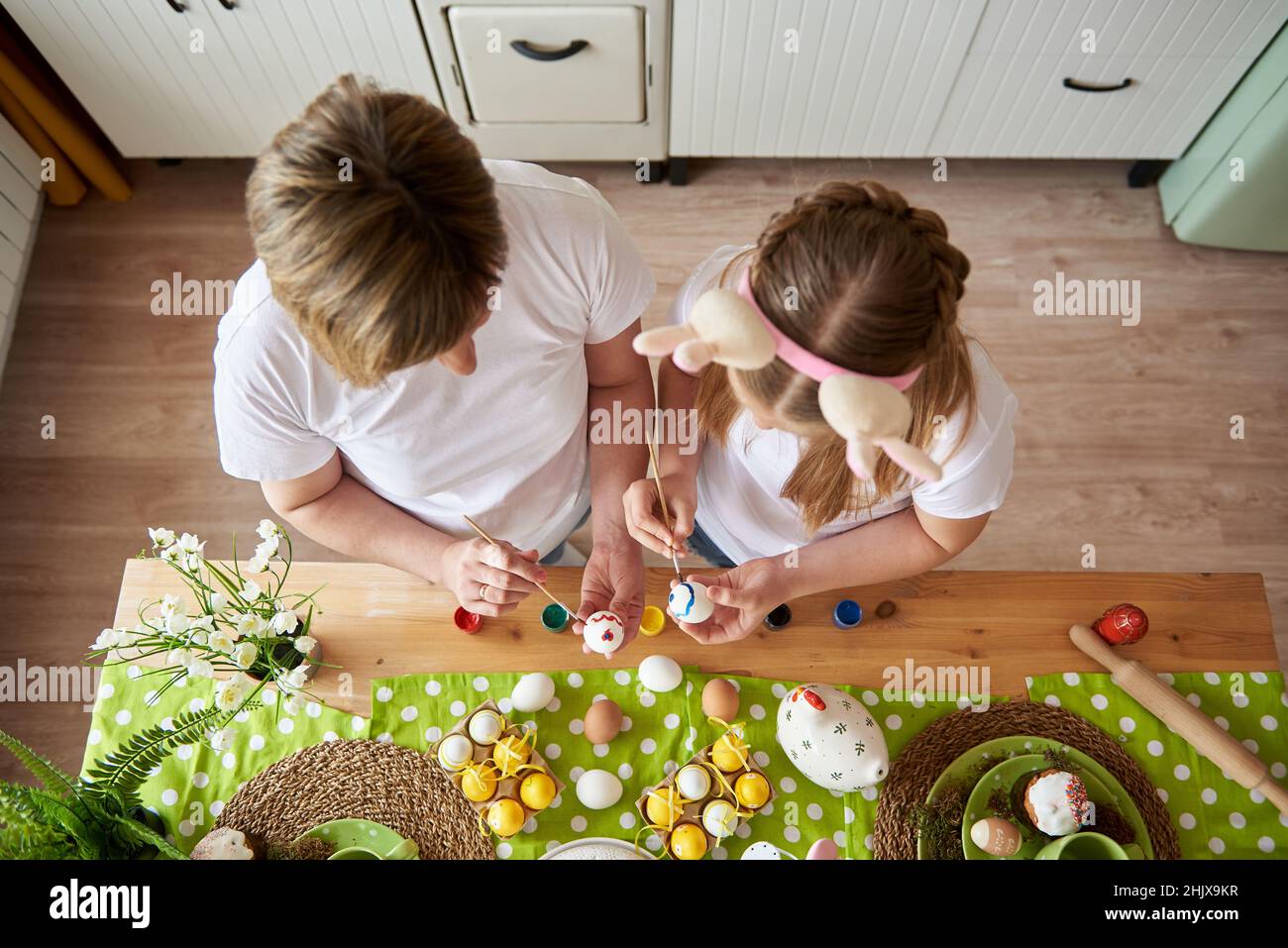 Maman et fille se préparent pour Pâques et peignent des œufs avec des pinceaux, vue du dessus. Banque D'Images