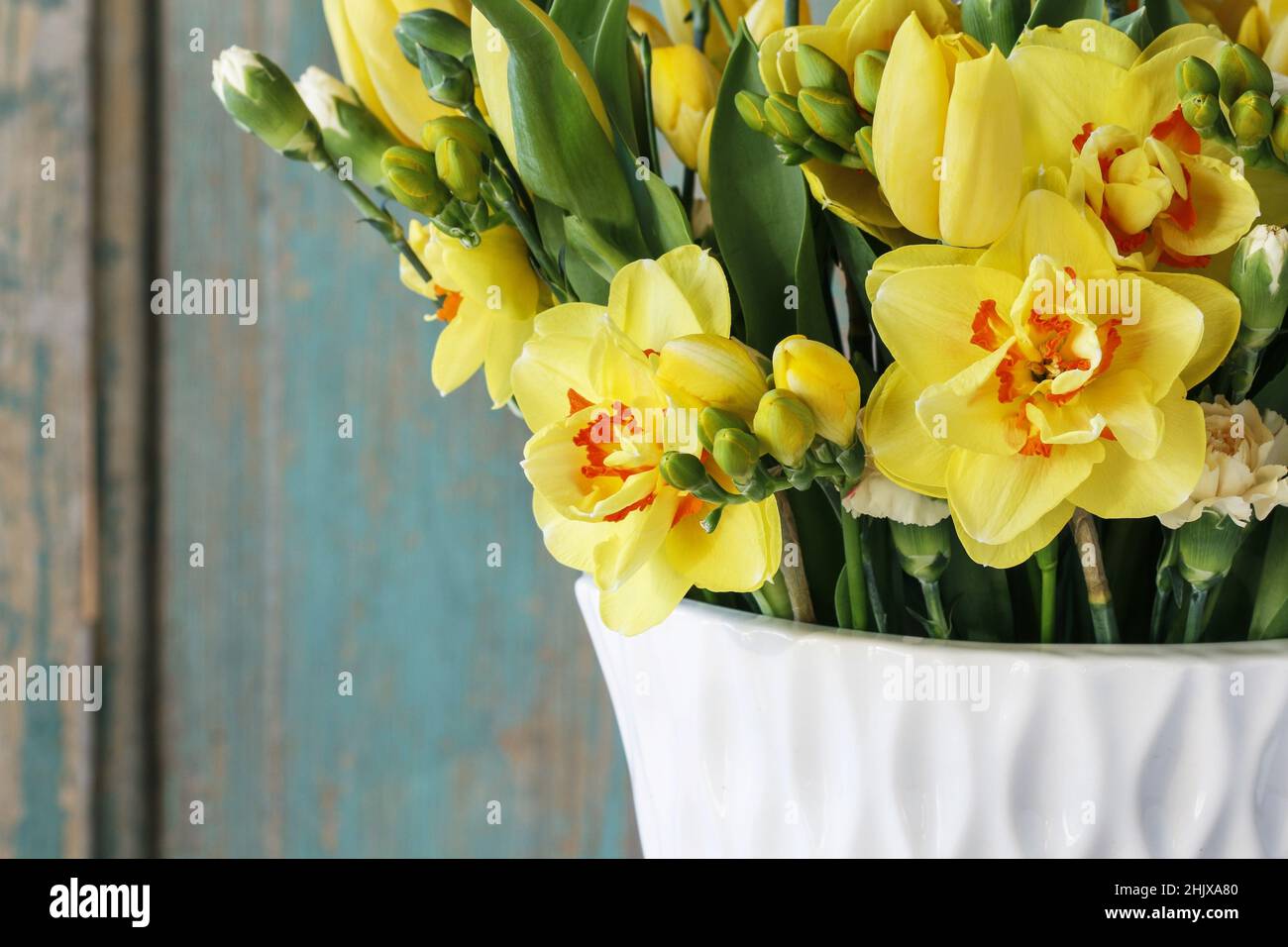 Bouquet de printemps avec tulipes jaunes, œillets et jonquilles. Fleurs fraîches dans un vase blanc. Banque D'Images