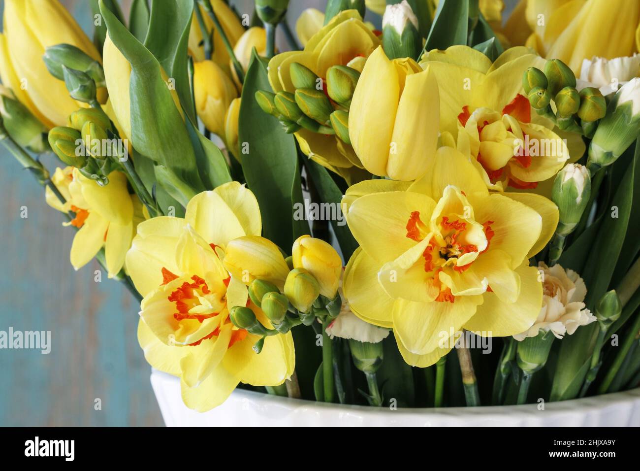 Bouquet de printemps avec tulipes jaunes, œillets et jonquilles. Fleurs fraîches dans un vase blanc. Banque D'Images
