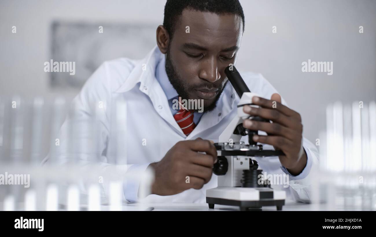 scientifique afro-américain en couche blanche regardant au microscope en laboratoire Banque D'Images