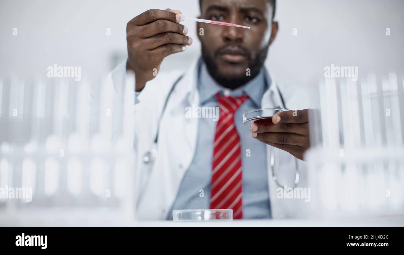 un scientifique afro-américain flou regarde la pipette avec du liquide rouge en laboratoire Banque D'Images