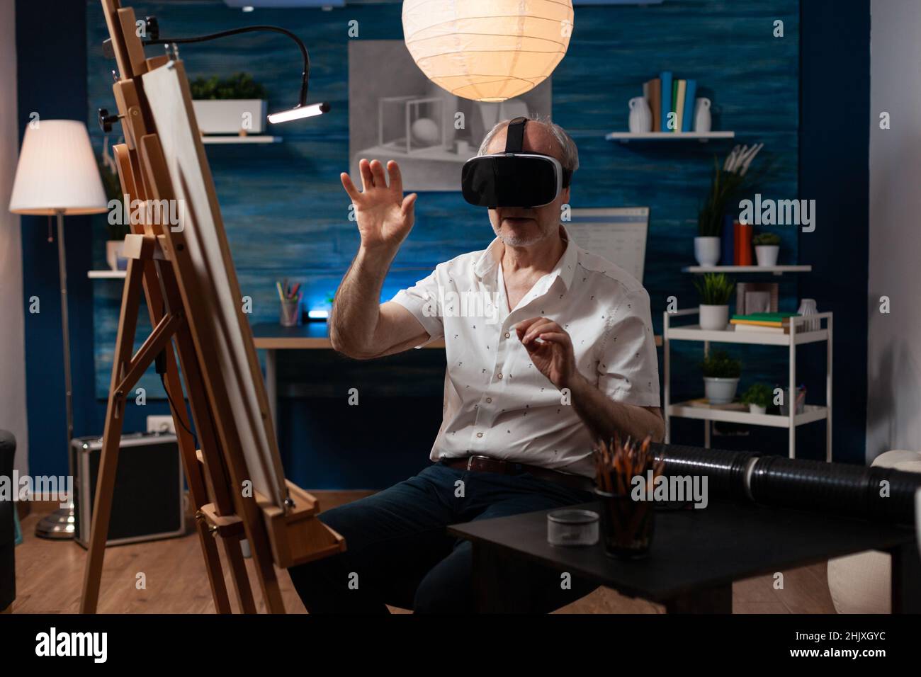 Artiste créatif retraité utilisant des lunettes de réalité virtuelle pour visualiser le modèle pour l'inspiration dans le studio d'art.Homme âgé utilisant des lunettes vr de technologie moderne pour améliorer les compétences de dessin. Banque D'Images