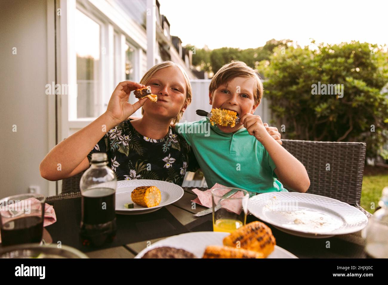 Portrait des frères et sœurs qui mangent du maïs grillé et de la viande tout en étant assis dans la cour arrière Banque D'Images