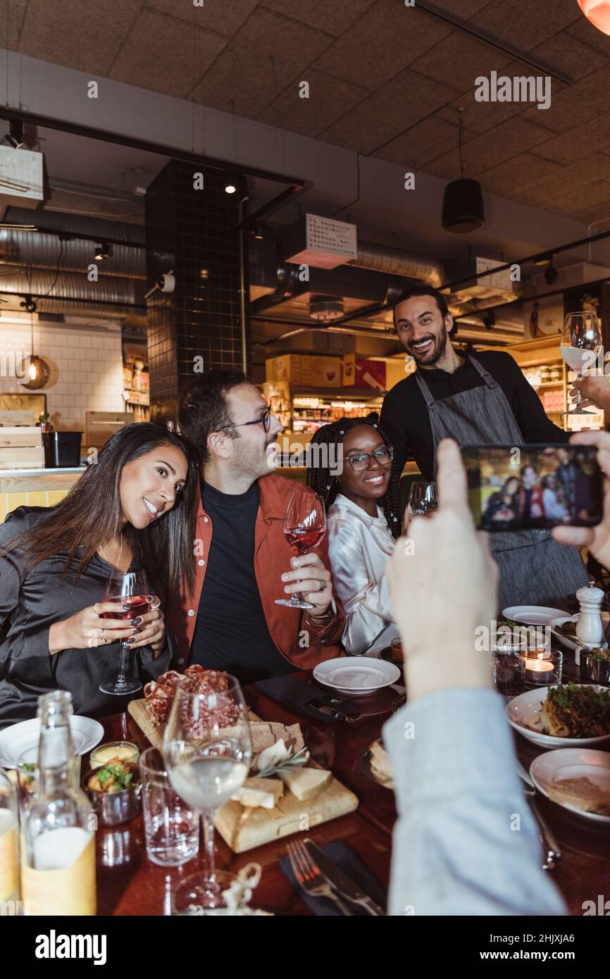 Image rognée d'un homme prenant des photos d'amis hommes et femmes à travers un smartphone dans le restaurant Banque D'Images
