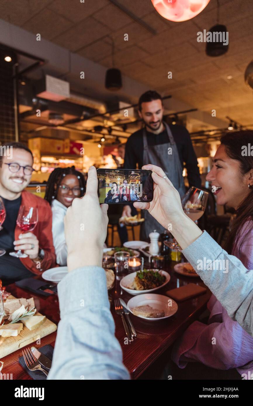 Image rognée d'un homme prenant des photos d'amis hommes et femmes par téléphone portable dans la barre Banque D'Images