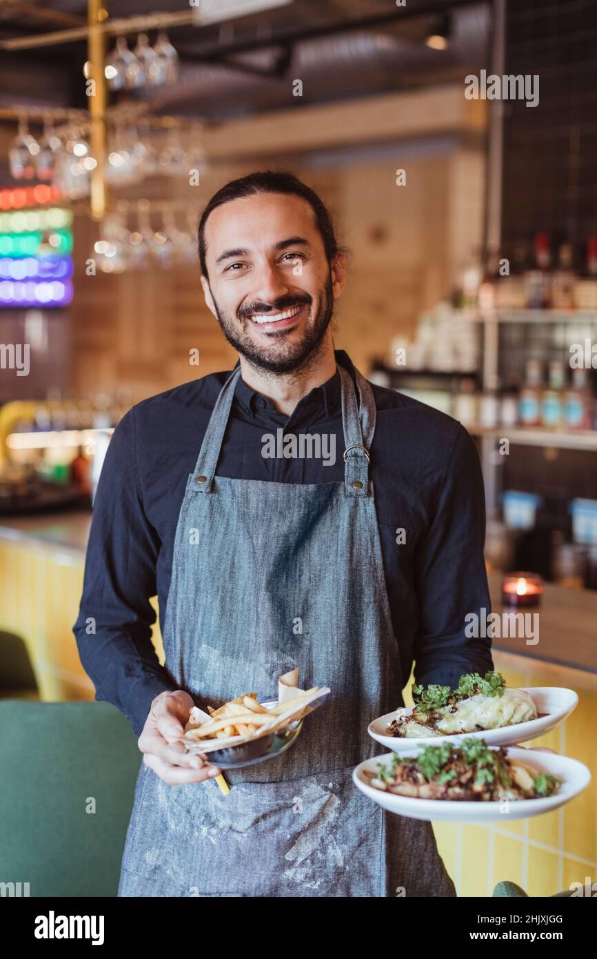 Portrait d'un serveur masculin souriant avec nourriture au restaurant Banque D'Images