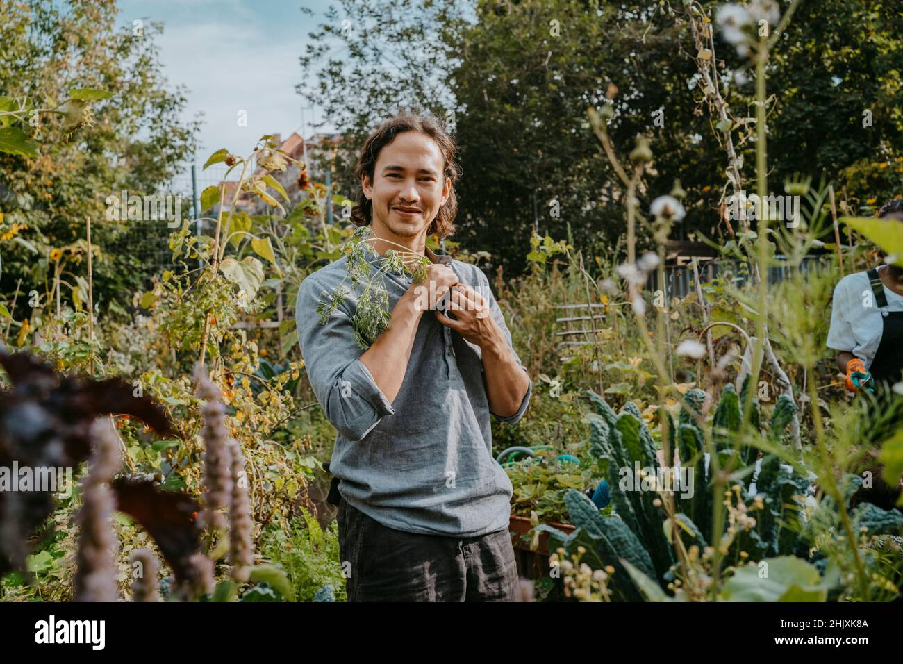 Portrait d'un homme souriant actionnaire agricole avec une plante dans un jardin urbain Banque D'Images
