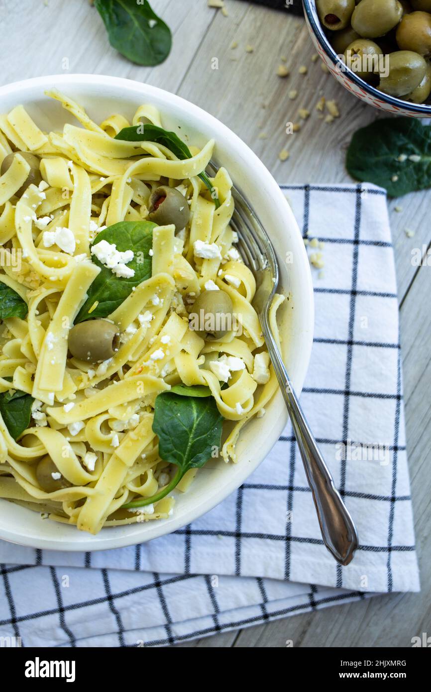 Tagliatelle au pesto avec feta et olives dans un bol blanc avec couverts, torchon et garniture. Banque D'Images