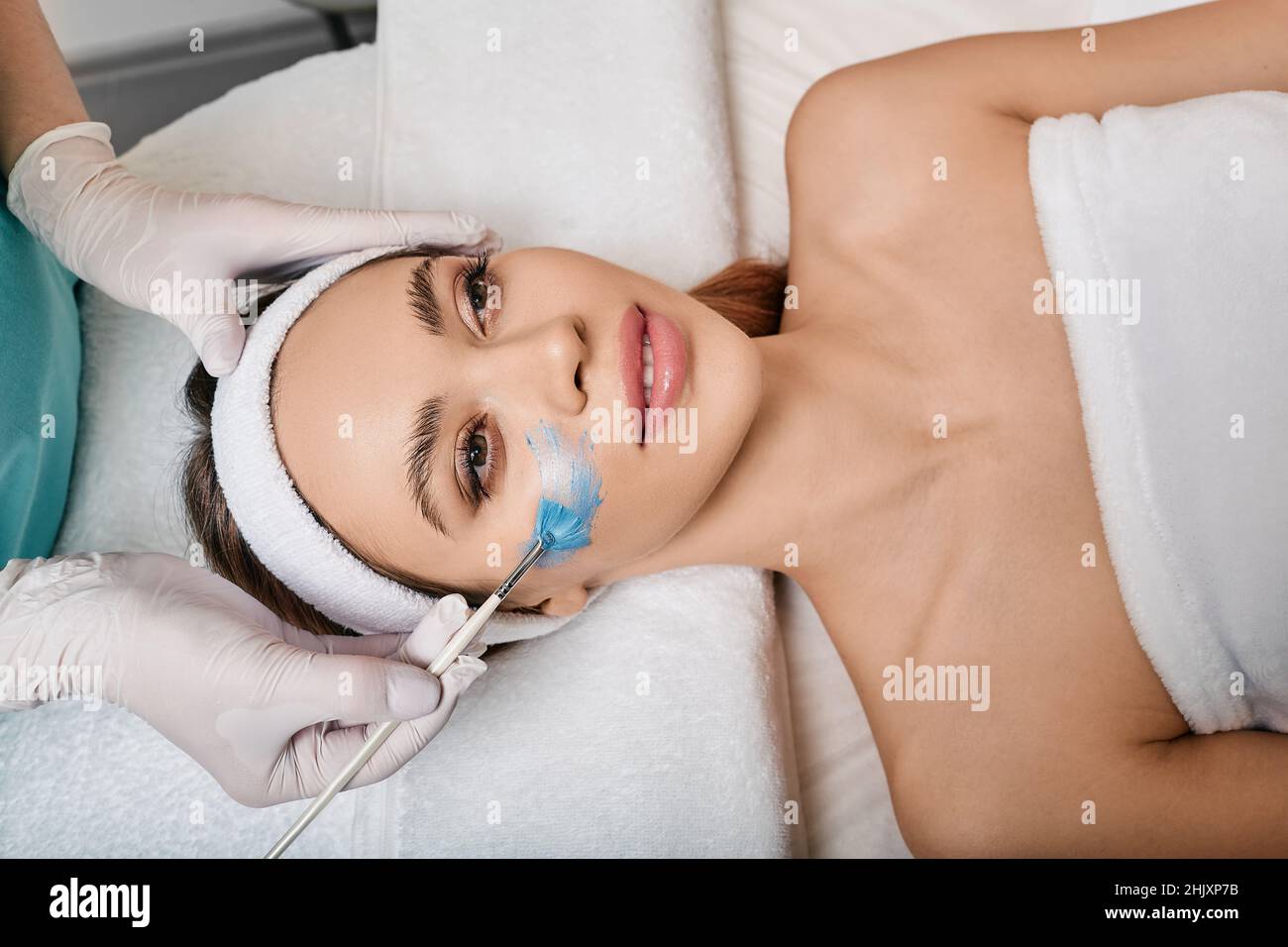 Femme pendant l'application du masque cosmétique de soins du visage avec esthéticienne couchée dans le salon de cosmétologie, vue d'en haut. soins de la peau du visage avec des mas cosmétiques Banque D'Images