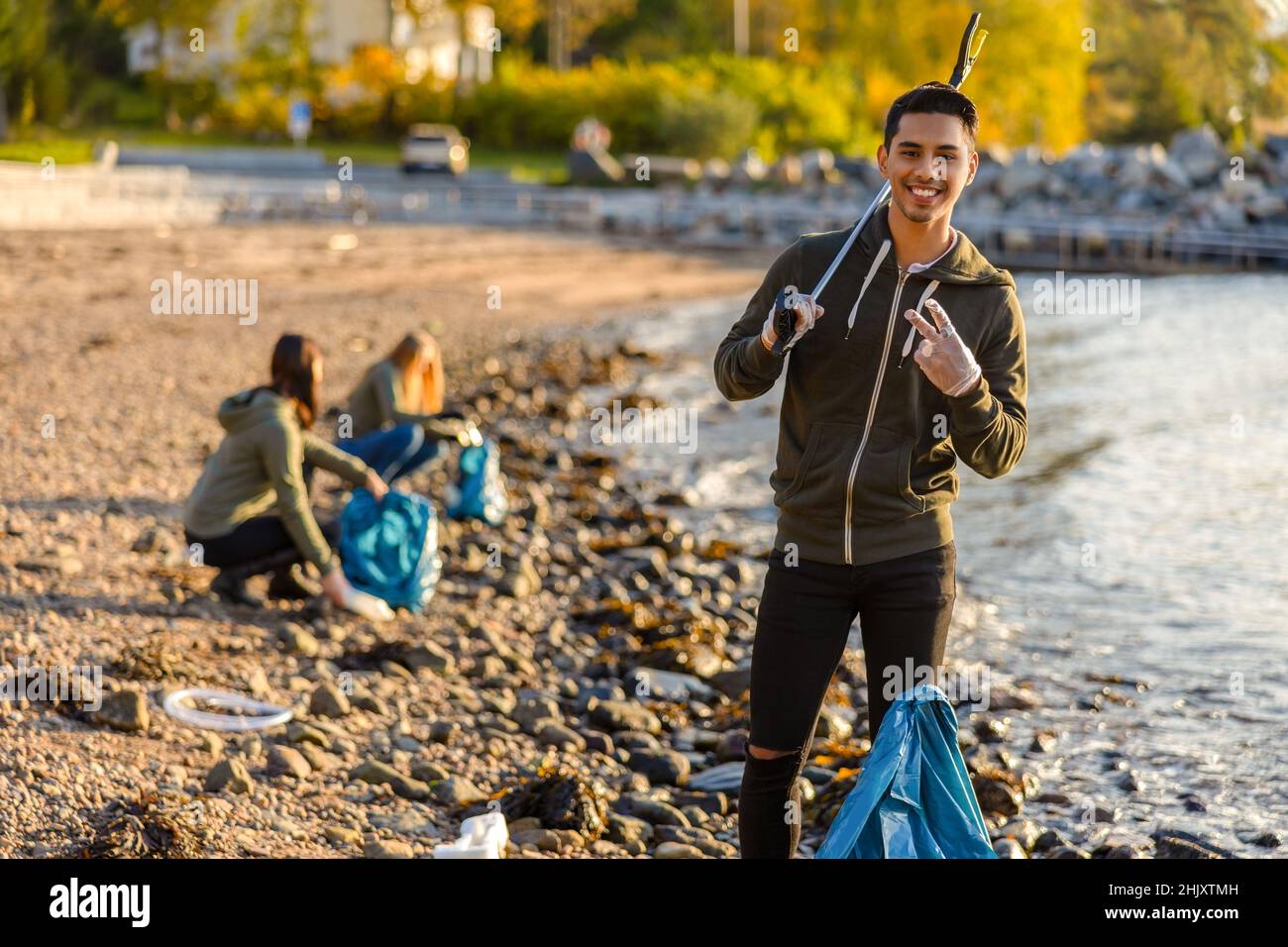 Fier homme nettoyant l'océan avec des bénévoles le jour ensoleillé Banque D'Images