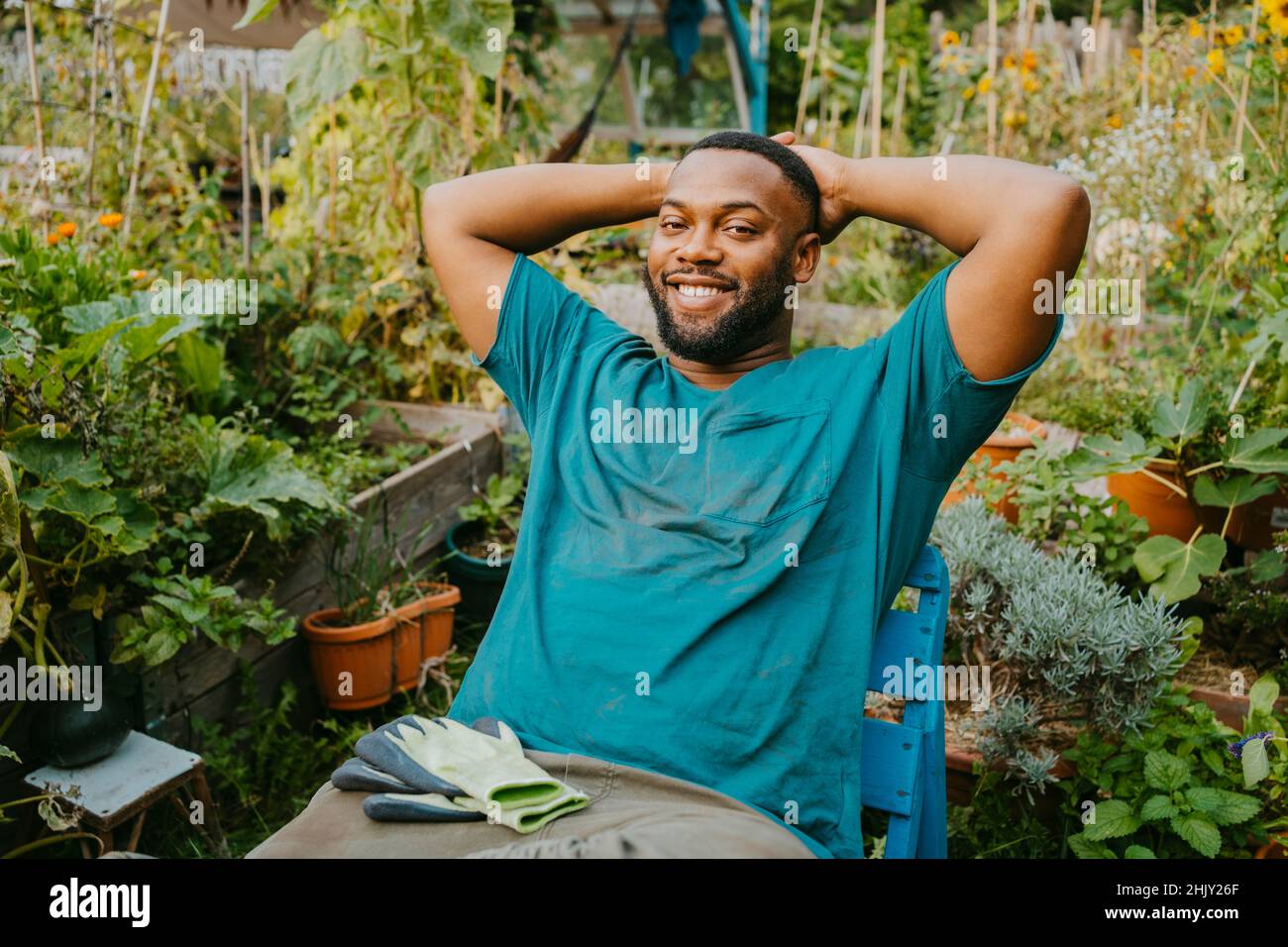 Portrait d'un homme bénévole souriant avec les mains derrière la tête assis dans le jardin communautaire Banque D'Images