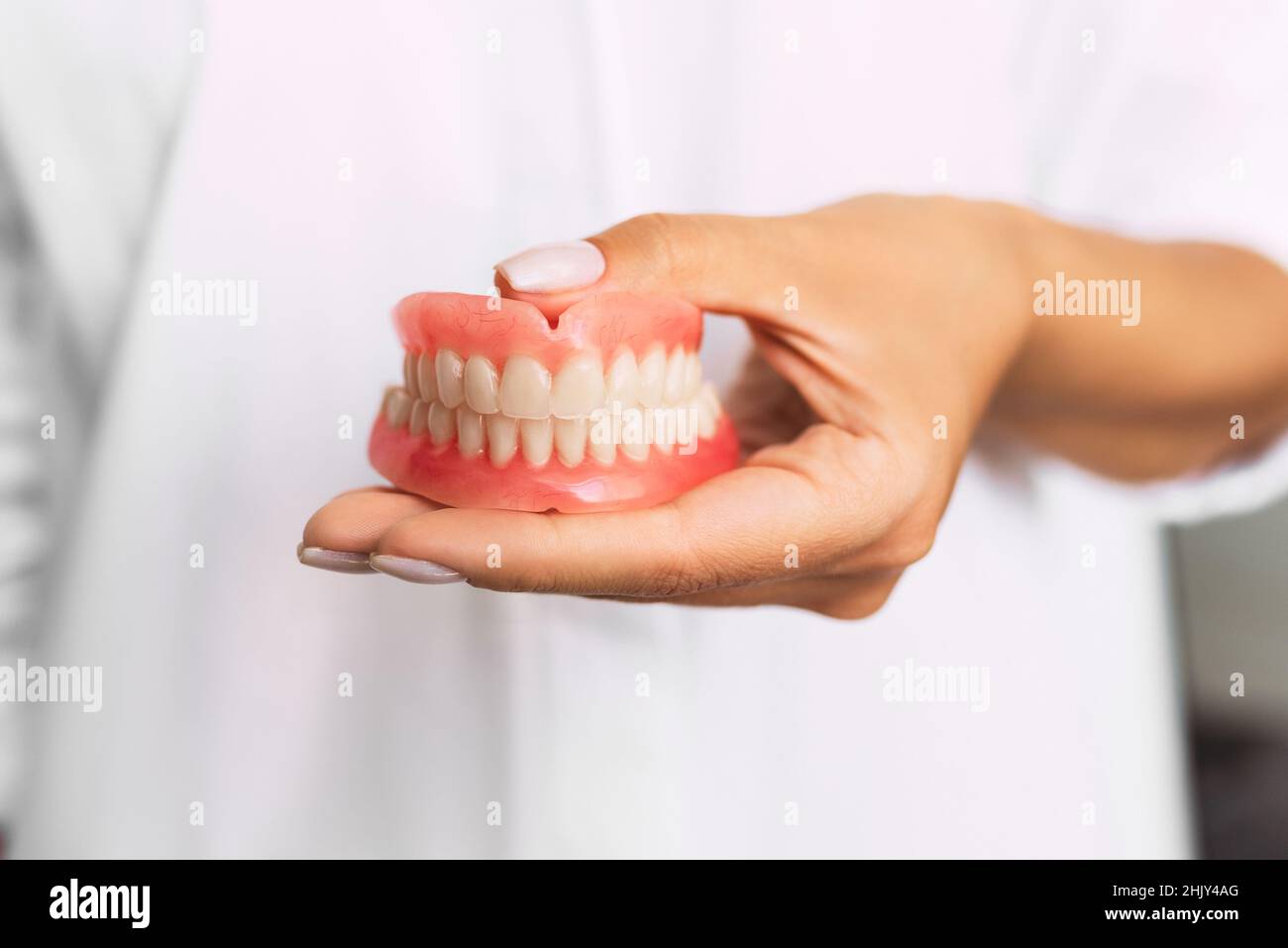 Prothèse dentaire dans les mains du médecin en gros plan.Dentiste tenant un pont dentaire en céramique.Vue avant de la prothèse complète.Pho conceptuel de la dentisterie Banque D'Images