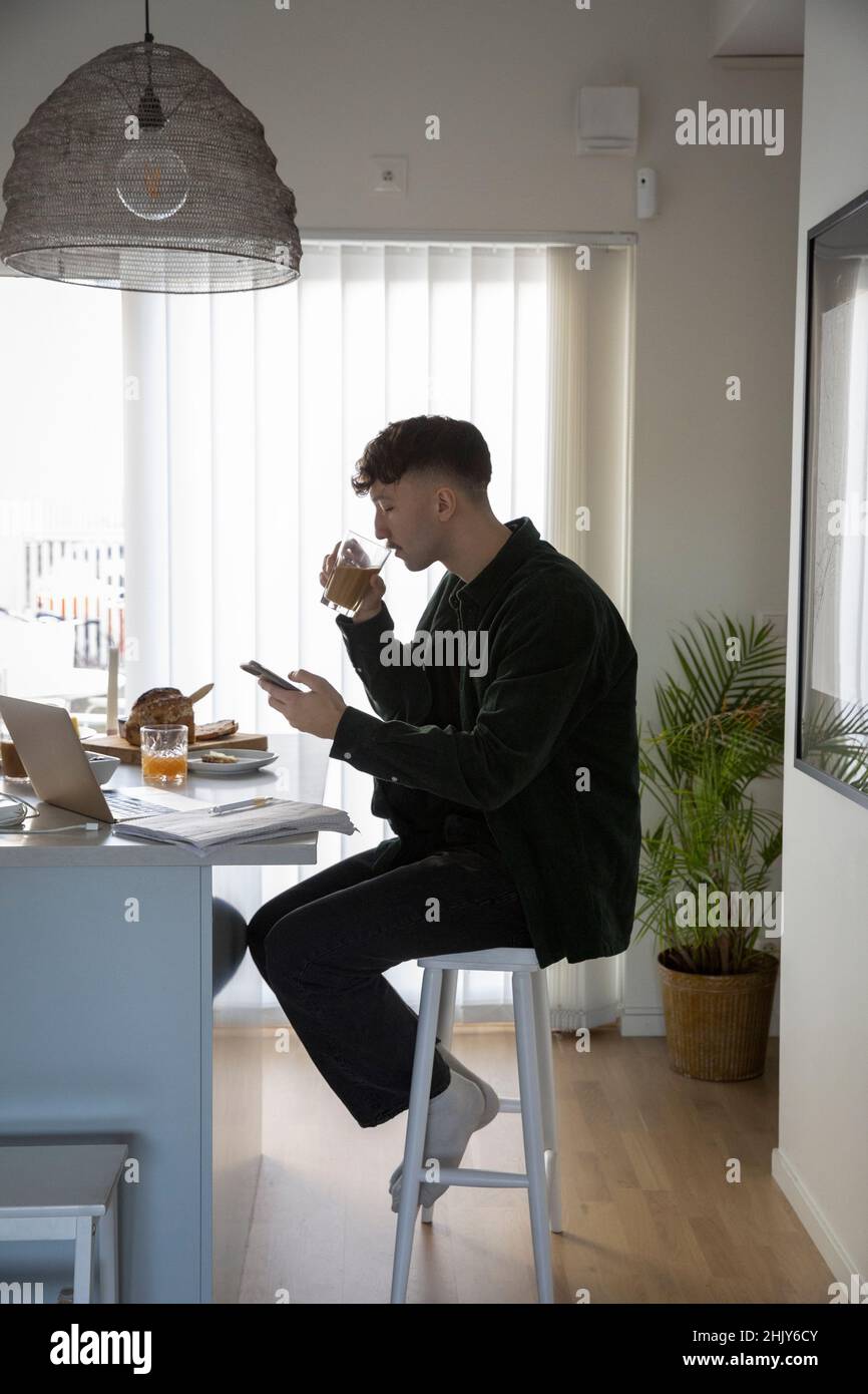Un jeune homme d'affaires qui boit à la maison à l'aide d'un smartphone Banque D'Images