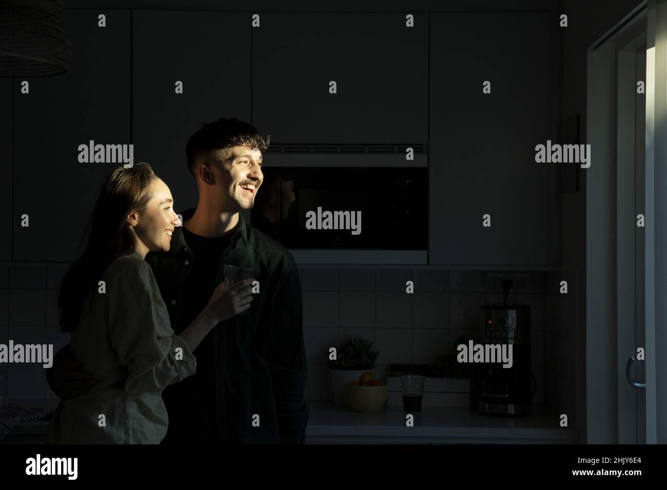 Un jeune couple heureux qui regarde loin en se tenant dans la cuisine Banque D'Images
