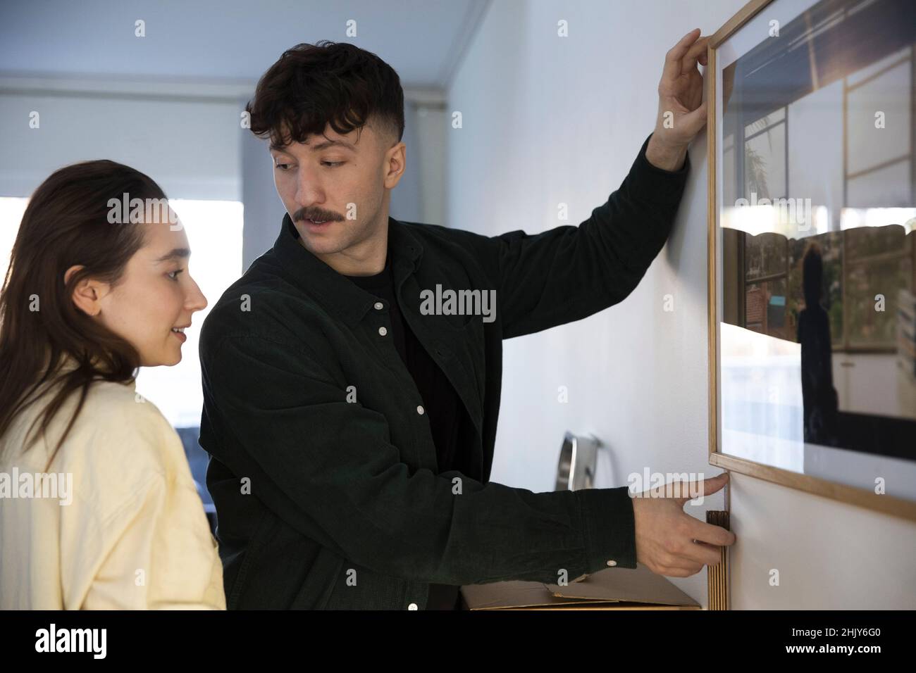 Homme discutant avec une petite amie tout en accrochant le cadre photo au mur dans le salon Banque D'Images