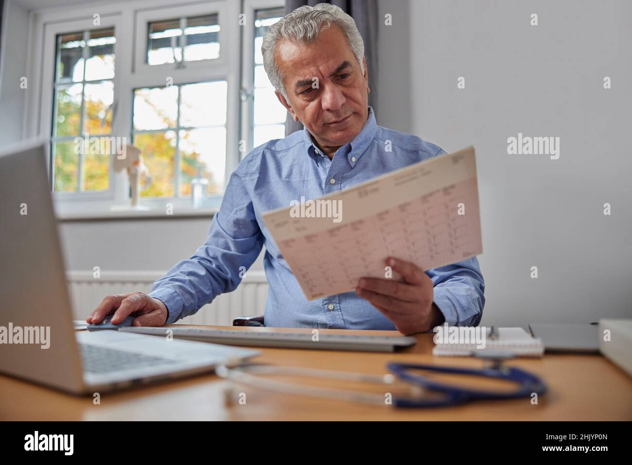 GP homme mature au bureau dans le bureau des médecins regarder la lecture de l'ECG Banque D'Images