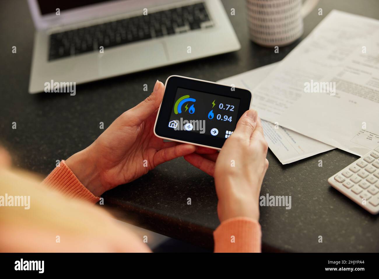 Gros plan d'une femme tenant un compteur d'énergie intelligent dans la cuisine mesure de la consommation d'électricité et de gaz avec des factures avec la calculatrice Banque D'Images