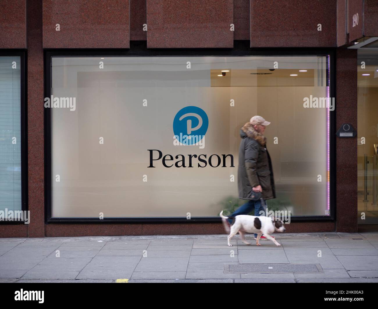 Homme avec chien marchant devant le siège de la société d'éducation Pearson dans le centre de Londres, Pearson plc est une société d'édition et d'éducation britannique qui possède des bureaux à Londres. Banque D'Images