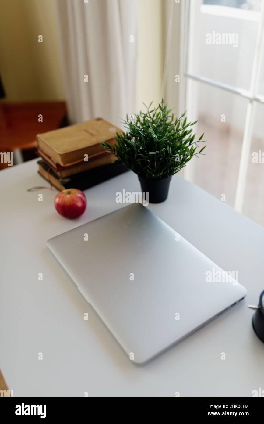 Ordinateur portable fermé, pomme, fleurs et vieille bibliothèque sur la table. Banque D'Images
