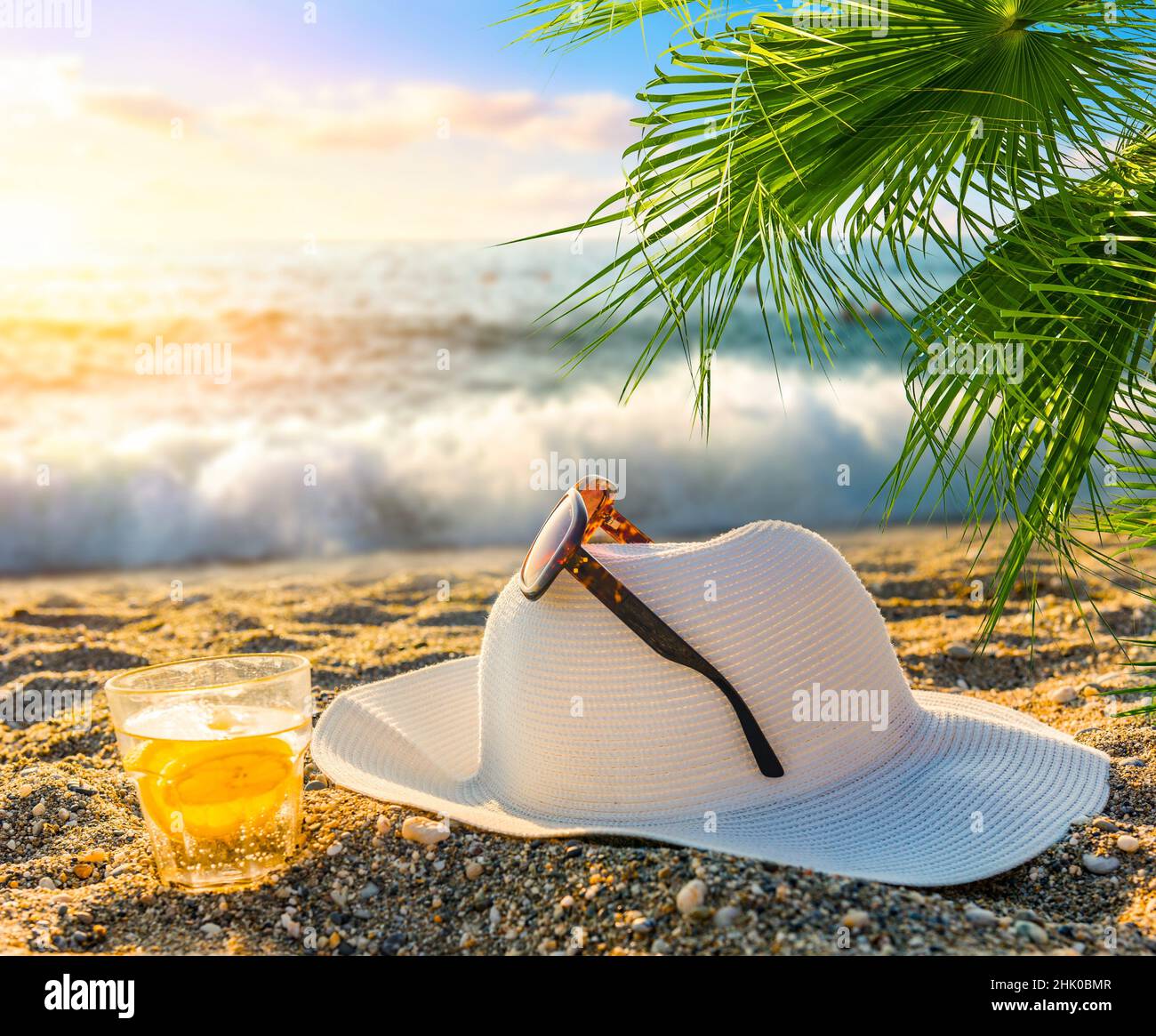 Chapeau avec lunettes de soleil et cocktail sur la plage au coucher du  soleil Photo Stock - Alamy