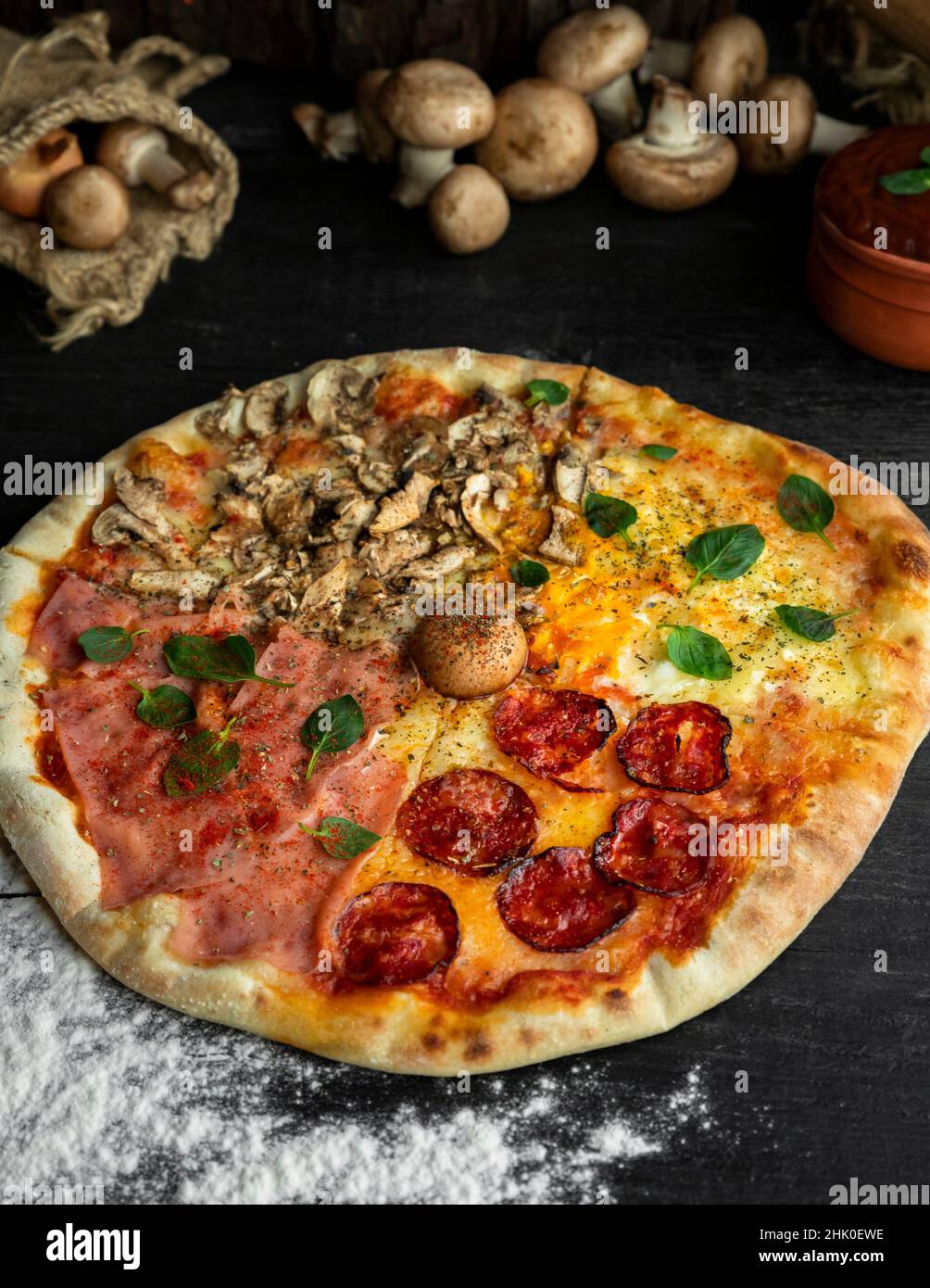 Pizza italienne four Seasons (Pizza Quattro Stagioni) avec différents ingrédients sur la table en bois dans la cuisine.Recettes italiennes faites maison. Banque D'Images