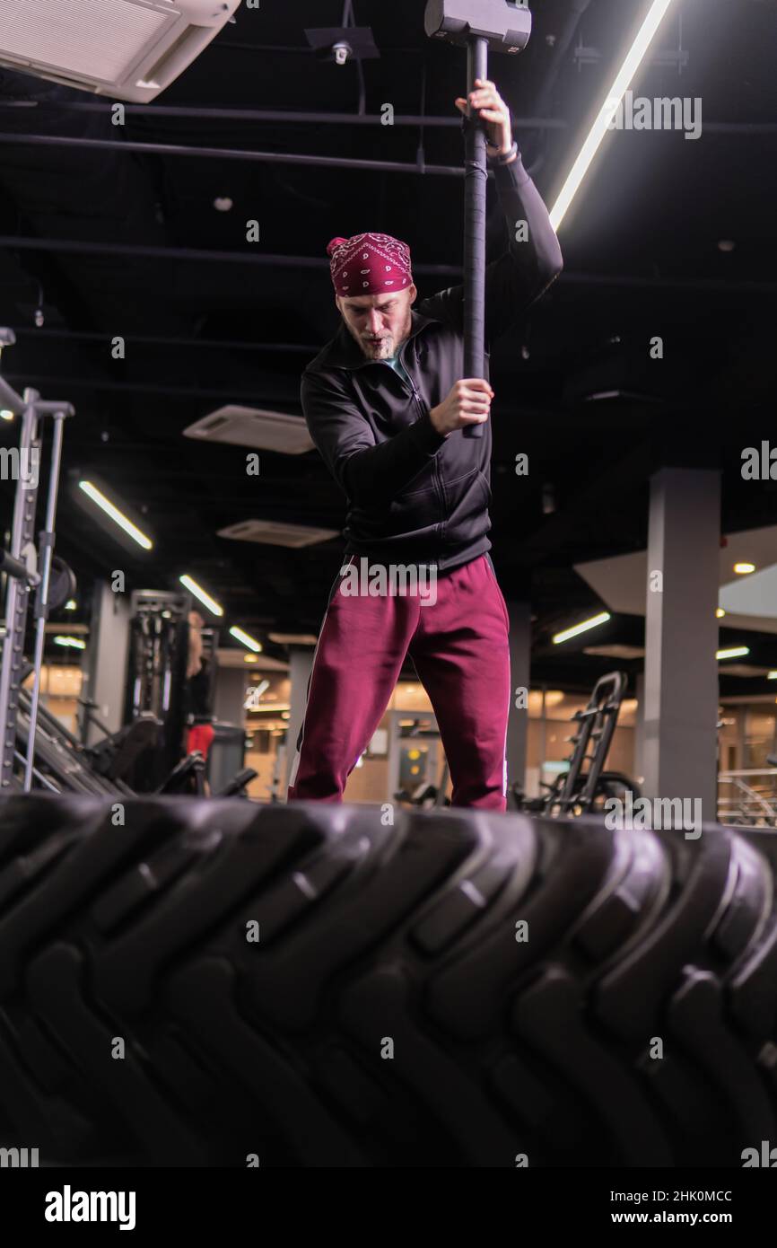Un homme frappe une roue de sledgehammer dans la forme physique, le concept d'un style de vie sain homme sledgehammer marteau actif, dans l'après-midi gym musculate i Banque D'Images