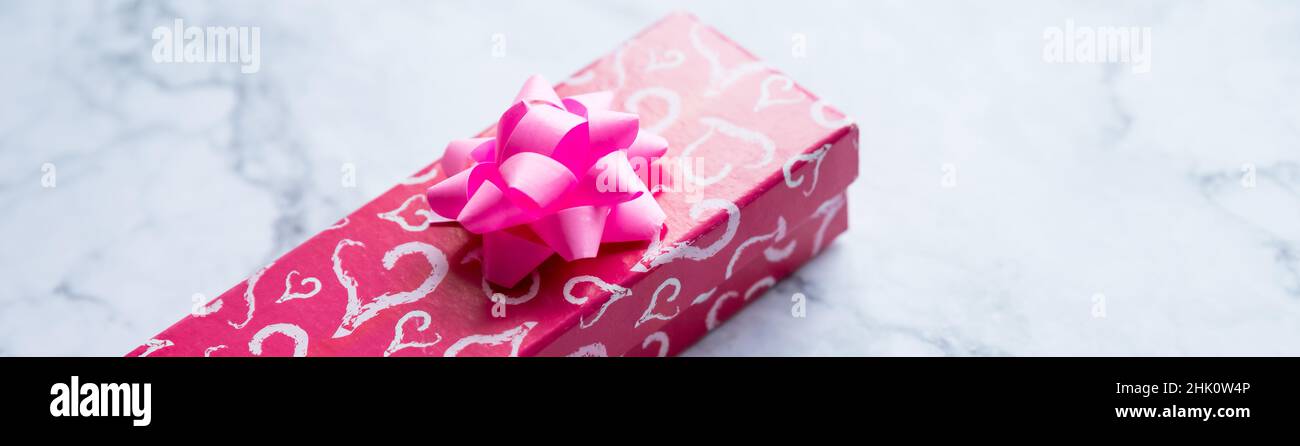 boîte cadeau rouge avec coeur rouge, noeud rose sur fond de marbre. Bannière Web des fêtes. Vue de dessus.style minimal, modèle de carte de vœux. Espace de copie Banque D'Images