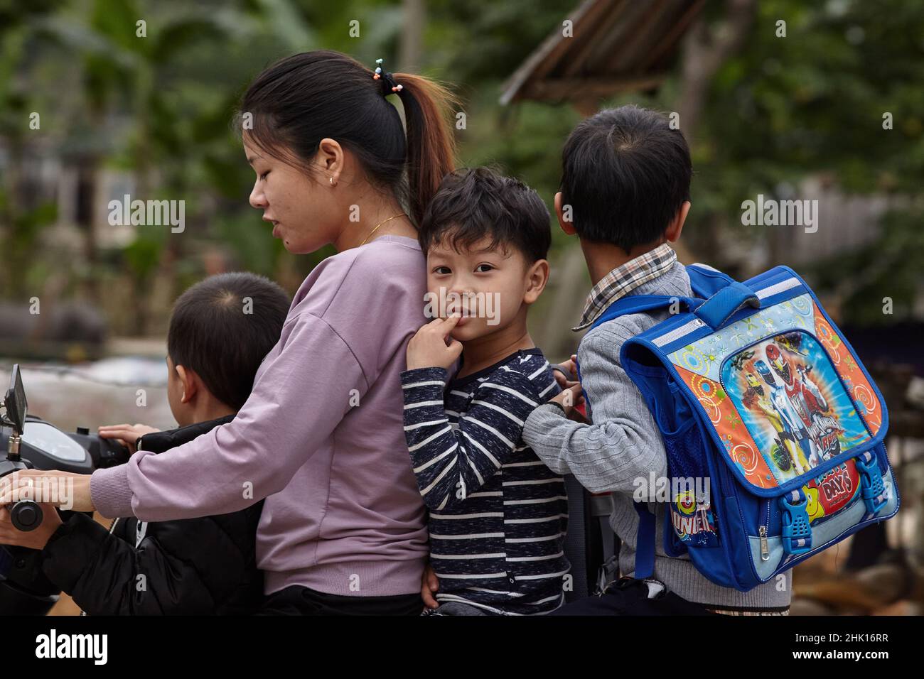 Un groupe de trois enfants avec une femme conduisent de l'école sur une moto . Banque D'Images