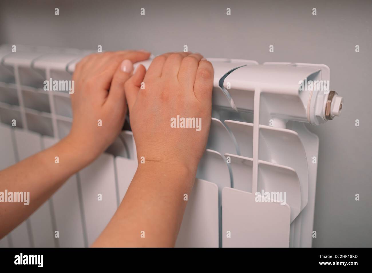 La femme touche à peine la batterie chaude pendant la saison de chauffage.Appareils de chauffage dans la maison, vue latérale Banque D'Images