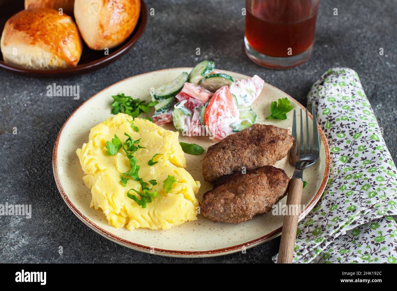 Côtelettes de viande maison avec pommes de terre machées et salade de légumes dans une assiette sur fond gris. Banque D'Images