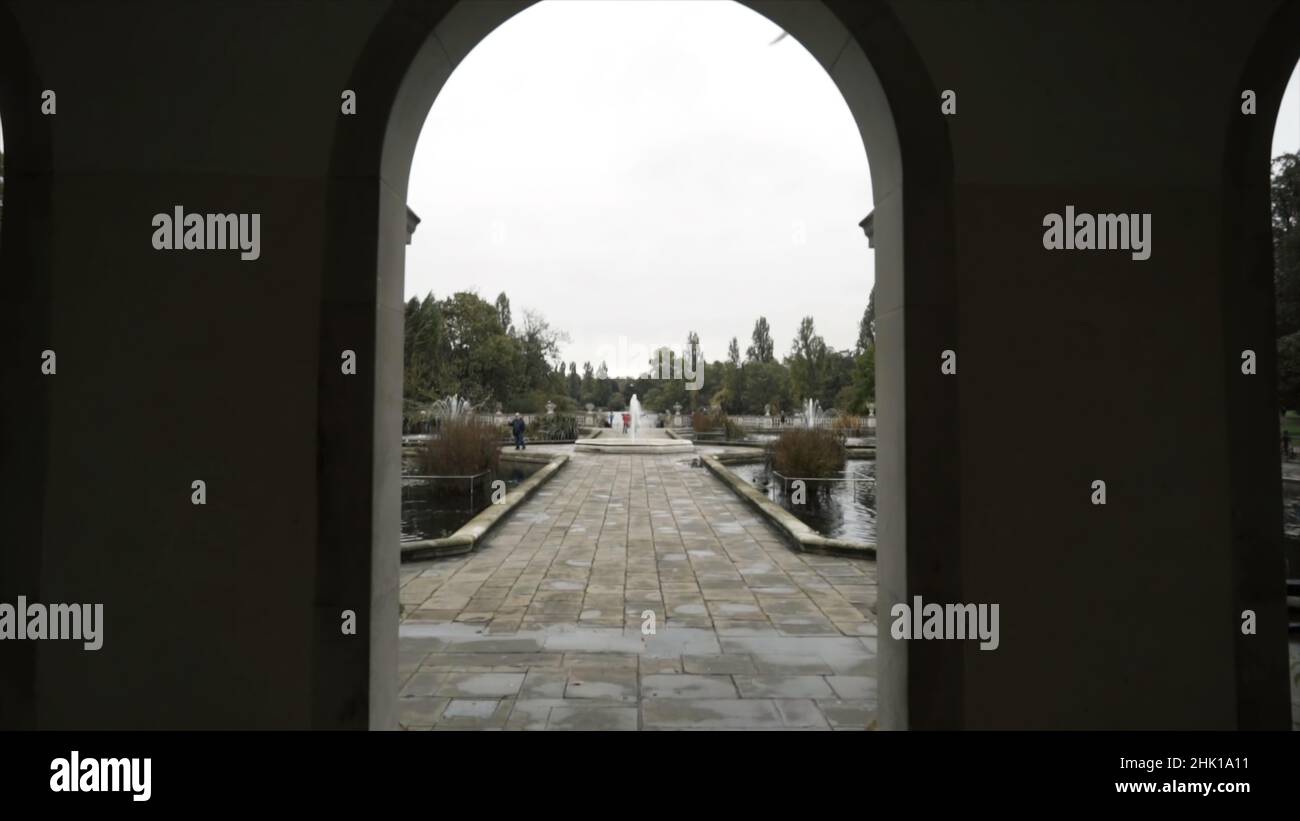 Vue de l'arche sur les personnes marchant dans un beau parc avec des fontaines et un étang contre le ciel gris nuageux.Entrée au parc Banque D'Images