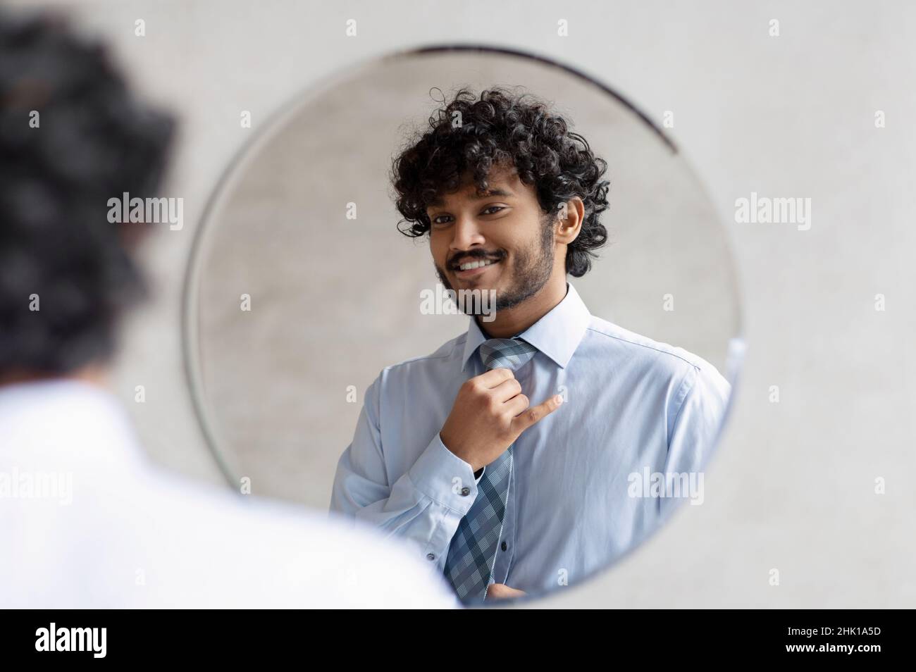 Beau homme d'affaires indien mettant sur la cravate et regardant son reflet dans le miroir, debout dans la salle de bains Banque D'Images
