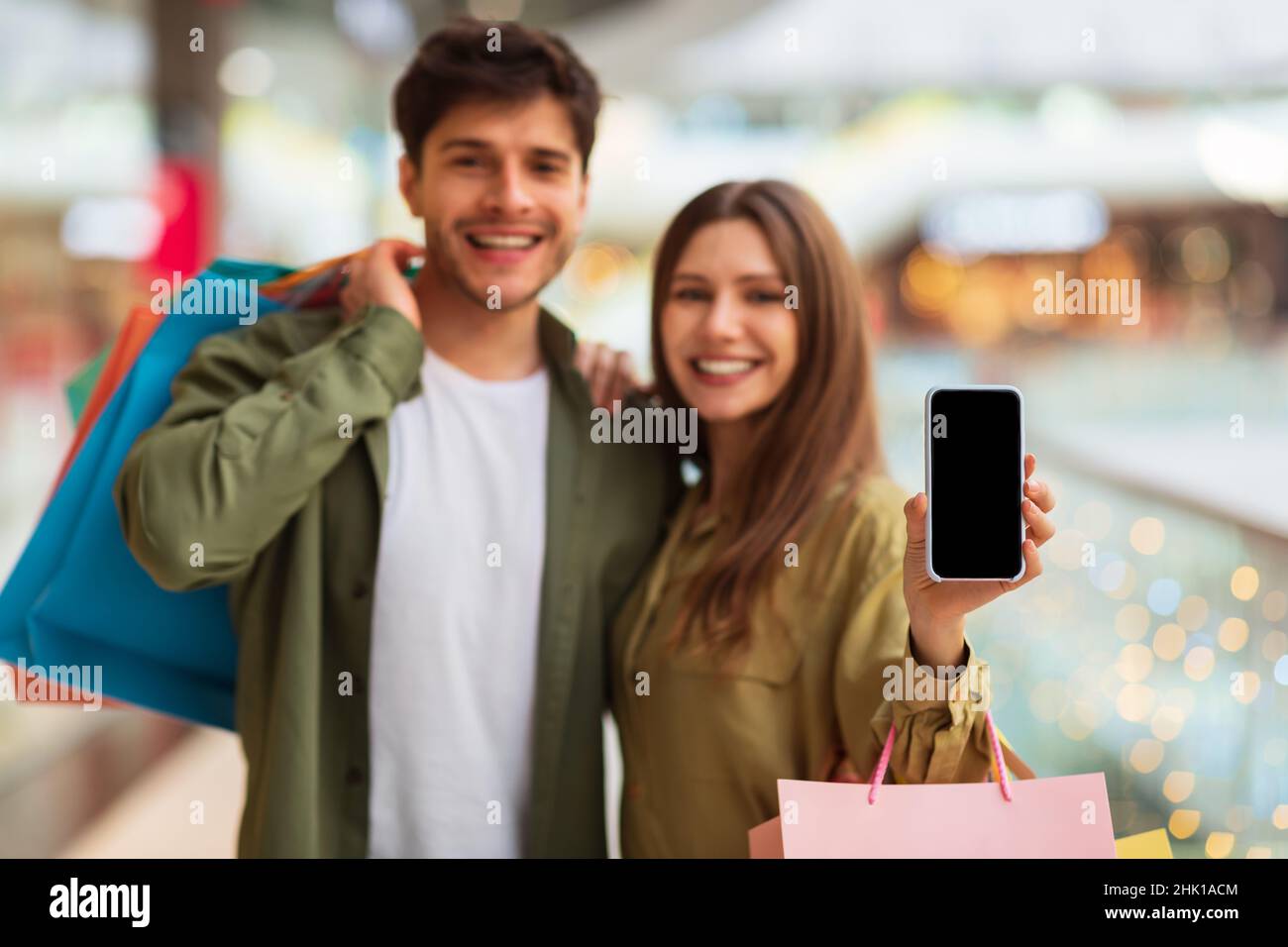 Couple montrant l'application de publicité par téléphone pour les achats mobiles dans le centre commercial Banque D'Images