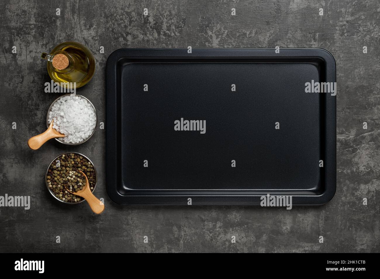 Vider la plaque de cuisson, le pot d'huile d'olive, le sel et les grains de poivre sur fond noir texturé.Plaque de cuisson rectangulaire et épices pour cuire et rôtir. Banque D'Images