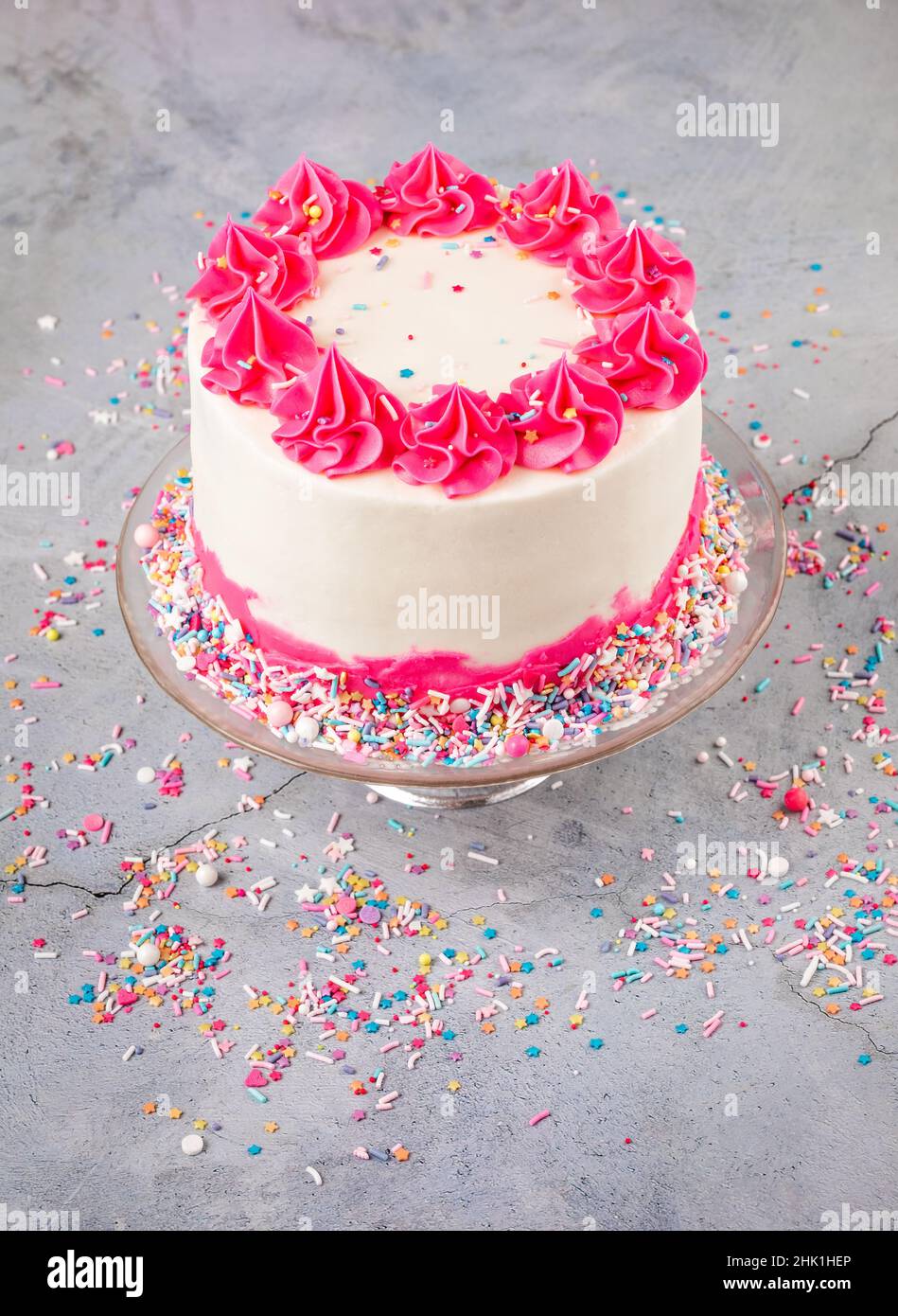 Gâteau d'anniversaire avec glaçage à la crème au beurre rose et blanc et saupoudrer de couleur sur un fond gris clair depuis le dessus de la tête. Banque D'Images