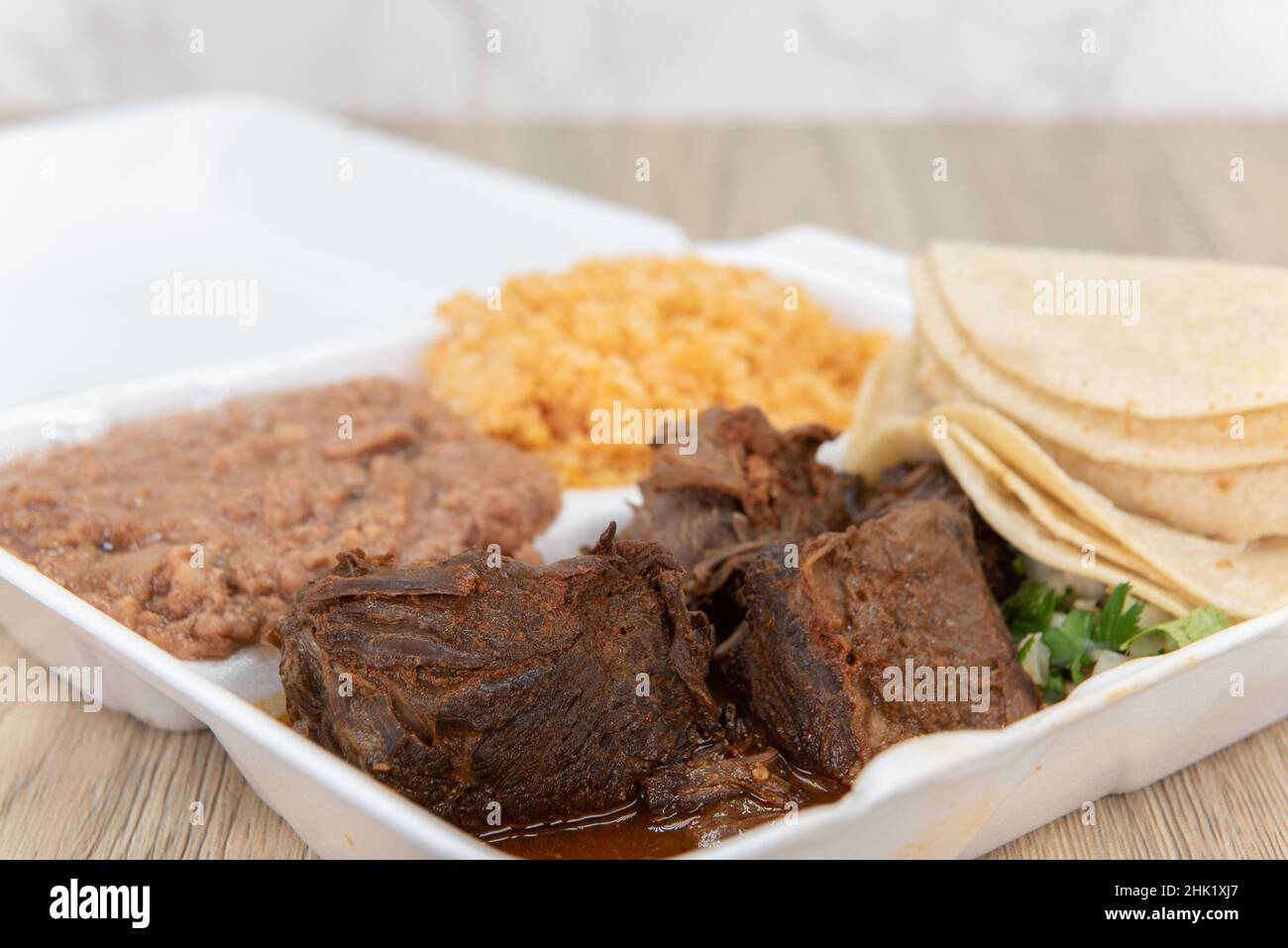 Une commande copieux de ragoût de birria servi pour faire des tacos avec les tortillas, le riz et les haricots inclus dans la boîte de styromousse. Banque D'Images
